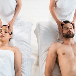 cropped view of masseurs doing massage to man and woman with closed eyes in spa center